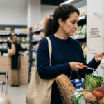 Shopper comparing grocery prices as inflation reduces household purchasing power.